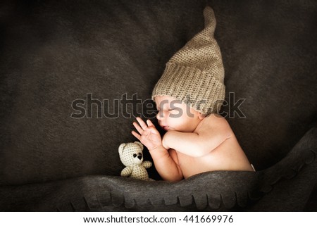 newborn baby sleeping with a toy next to the knitted teddy bear