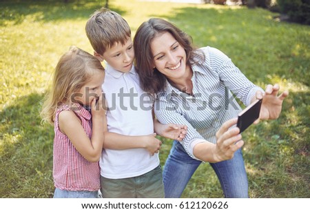 A young mother with children walks in the park and does selfie with them. Mom's daughter and son on a walk