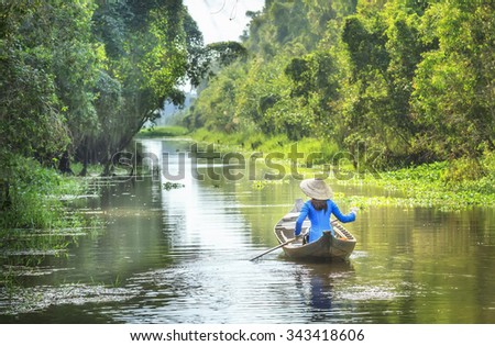 In Dong Thap, Vietnam - January 14th, 2014: Woman rowing on river passed house homeland with small body, shirt Ba Ba and conical hats typical of Southeast women in spring afternoon Dong Thap, Vietnam