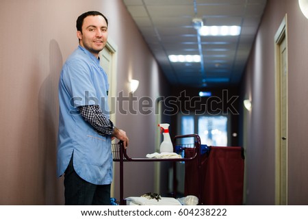 A man who is on the hotel cleaning crew staff is smiling with a towel vacuum in the process of cleaning the hotel rooms and delivering top-knotch service to the guests.