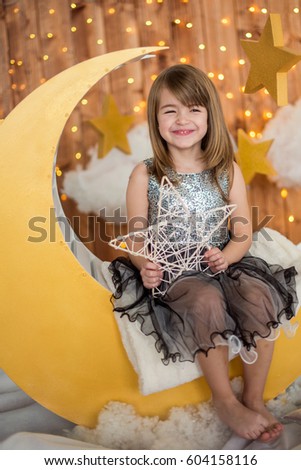 Little cute girl sitting on a wooden month with a decorative star in her hands. Children's photozone.