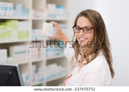 Smiling attractive young female pharmacist promoting a product in a blank white box she is holding up in her hand in the pharmacy