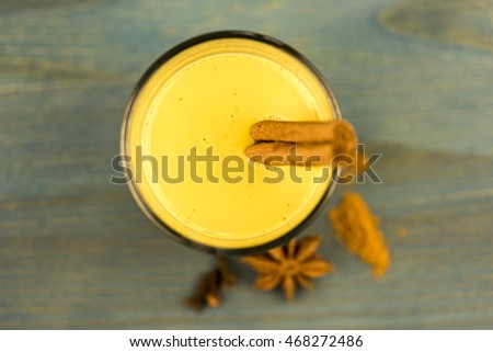First person perspective top down view on turmeric latte with cinnamon sticks and anise herb on wooden table