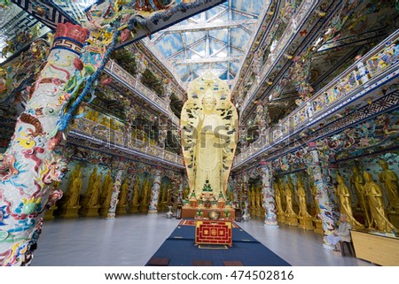 NHA TRANG, VIETNAM - JUNE 23, 2016: Internal furniture of the Buddhist temple. Gold statue of Buddha in the middle of the hall. Walls are painted with multi-colored drawings.