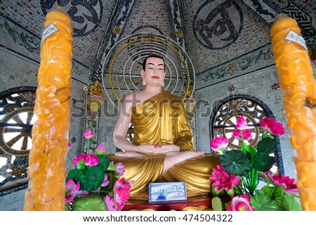 NHA TRANG, VIETNAM - JUNE 23, 2016: Big statue of Buddha in a gold cape inside the temple. Nearby there are two big candles and beautiful flowers