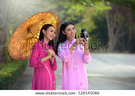 Asian woman wearing a dress of Vietnamese Ao dai is carrying a camera.