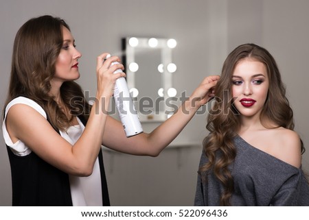 Hairdresser using hairspray on client's hair at salon, two beautiful women