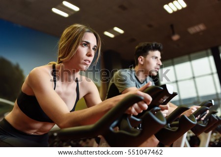 Attractive woman and man biking in the gym, exercising legs doing cardio workout cycling bikes. Couple in a spinning class wearing sportswear.