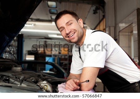 Portrait of handsome mechanic based on car in auto repair shop smiling