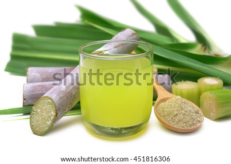 Fresh squeezed sugar cane juice in clear glass with cut pieces cane and brown sugar on white background.