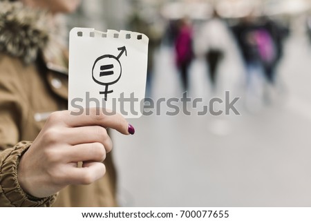 closeup of a young caucasian woman in the street showing a piece of paper with a symbol for gender equality drawn in it