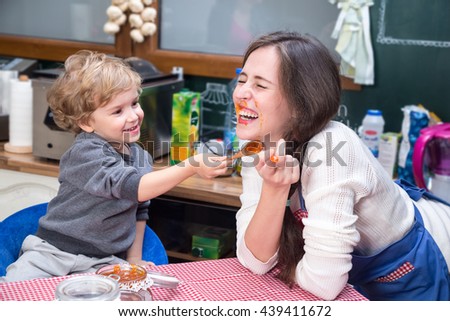 Happy mother and son laughing during breakfast. He is smudging jam on woman's face.