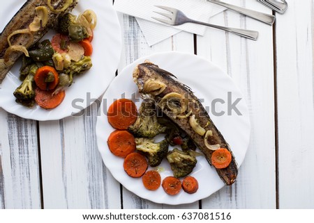 Baked roasted fried fish with baked, baked, gifted vegetables on a white wooden table