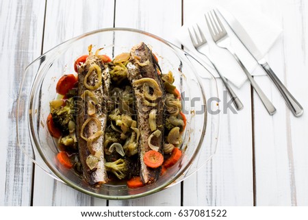 Baked roasted fried fish with baked, baked, gifted vegetables on a white wooden table