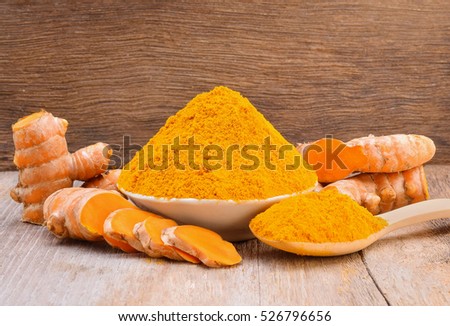 Turmeric roots with turmeric powder on wooden background