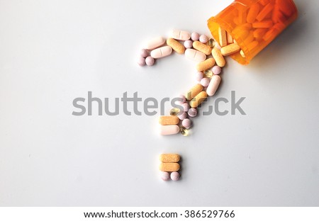 different drugs and health supplement pills in a question mark poured from a medicine bottle
