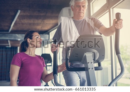 Senior man exercising on stationary bikes in fitness class. Man workout in gym. Senior with personal trainer.