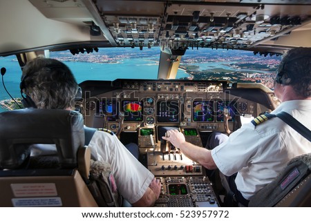 The cockpit of modern jet airplane. Aircraft flies above the city landscape and river. Pilots at work.