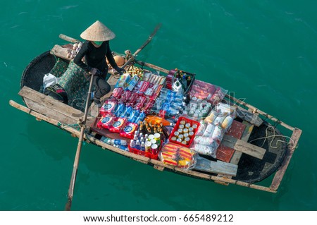 HALONG BAY, VIETNAM - NOVEMBER 23, 2009: Vietnamese saleswoman with conical hat and her goods rowing on the green emerald waters of Halong Bay in the South China Sea.