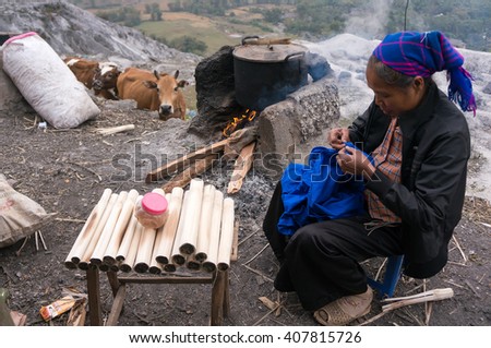 HOA BINH, Vietnam, January 12, 2016 Thai ethnic woman, sits embroidery, the pot of food, with a cow in the distance stood watching. peaceful scene
