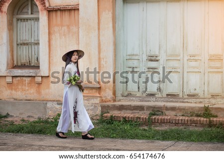 Beautiful woman wearing a Vietnamese dress Ao Dai holding lotus In abandoned buildings.