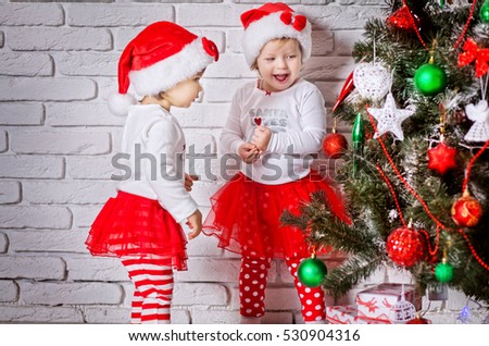 Two little adorable girls in red santa's suit standing near christmas tree and having fun. Children happy. New year photo.