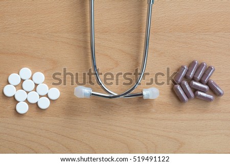 Comparing many pills of conventional or modern medicine versus many capsule of traditional,alternative, herbal elderberry medicine on wooden background with doctor medical stethoscope.