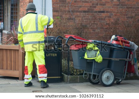 street sweeper collecting litter with street barrow in reflective gear and placing it in bin