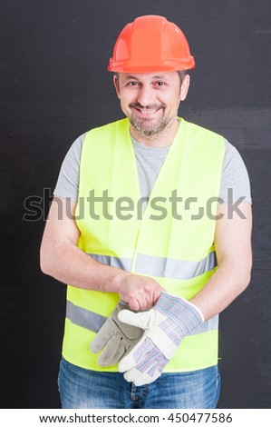Happy attractive constructor getting ready for work and putting gloves on isolated on black background