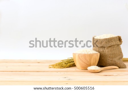 White rice in bowl and a bag, a wooden spoon and rice plant on a wooden table, Isolated in a white background, Side view with copy space