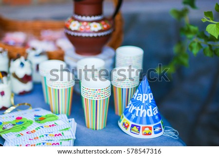Photo fragment table decoration for children's parties, birthday against backdrop of orange brick wall. On photo depicts clay jug, wicker basket, multicolored striped cardboard cups for drink