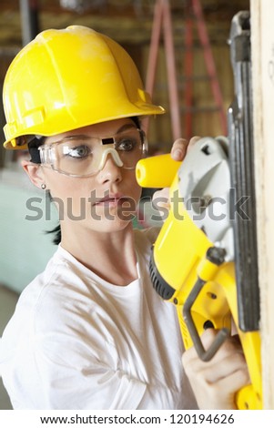 Serious female construction worker cutting wood with a power saw