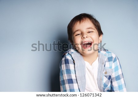 Portrait of happy joyful laughing beautiful little boy on blue background