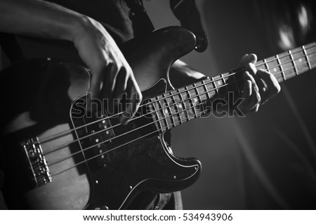 Closeup photo of bass guitar player hands, soft selective focus, live music theme, black and white