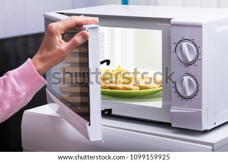 Close-up Of Woman Heating Fried Food In Microwave Oven At Home