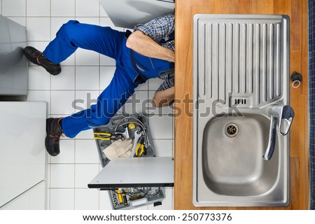 Male Plumber Examining Sink In Kitchen Holding Clipboard
