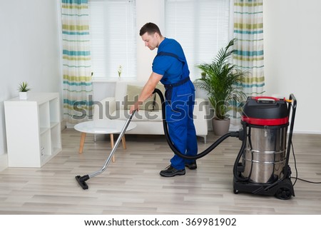 Full length of male worker cleaning floor with vacuum cleaner at home
