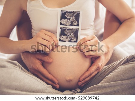 Cropped image of beautiful pregnant woman and her handsome husband holding a sonogram