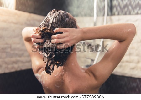 Back view of beautiful naked young woman washing her hair while taking shower in bathroom