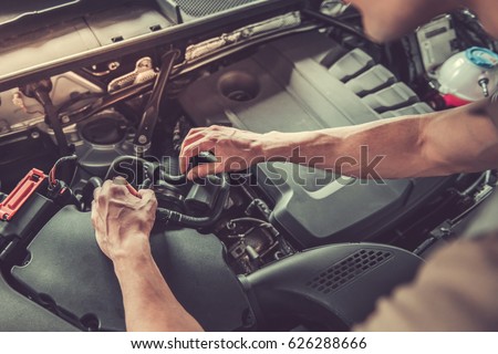 Cropped image of handsome young auto mechanic in uniform repairing car in auto service