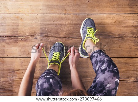 Unrecognizable young runner tying her shoelaces. Studio shot on wooden floor background.