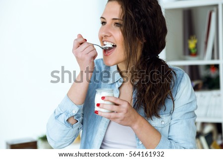Portrait of beautiful young woman eating yogurt at home.
