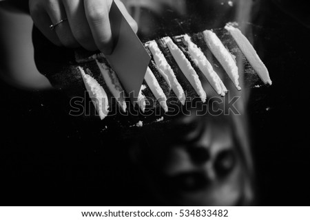 cocaine or other drugs cut with card on mirror with female reflection, hand dividing white powder narcotic, monochrome