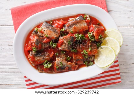 Braised sardines in tomato sauce with lime and parsley close-up on a plate. Horizontal view from above