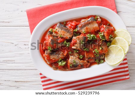 sardines in tomato sauce, decorated with lime and parsley close-up on a plate. horizontal view from above