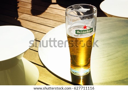 AMSTERDAM, NETHERLANDS - APR 08, 2017 : Glass with Heineken Lager Beer on outdoor bar table on sunny day. Heineken is the flagship product of Heineken International