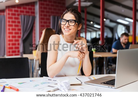 Portrait of smiling pretty young business woman in glasses sitting on workplace
