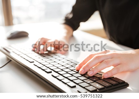 Cropped photo of young woman worker sitting in office while typing by keyboard.