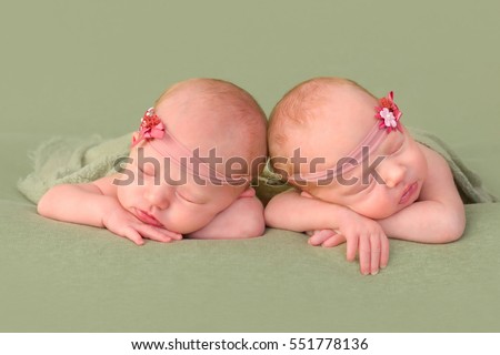3 weeks old identical twin girls sleeping on a green backdrop