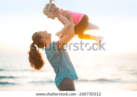 Mother throwing baby up on beach in the evening - stock photo